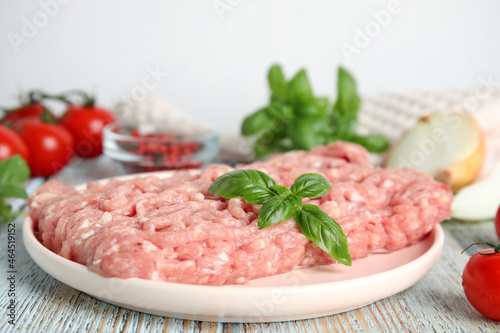 Raw chicken minced meat with basil on light blue wooden table, closeup