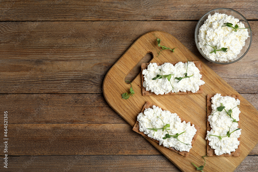 Crispy crackers with cottage cheese and microgreens on wooden table, flat lay. Space for text