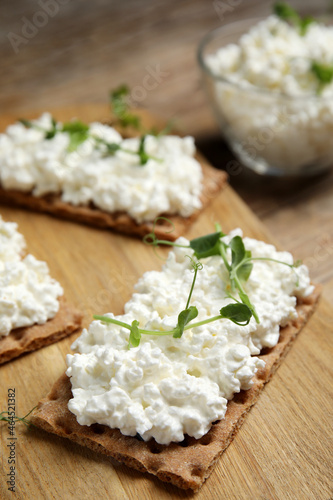 Crispy crackers with cottage cheese and microgreens on wooden board, closeup