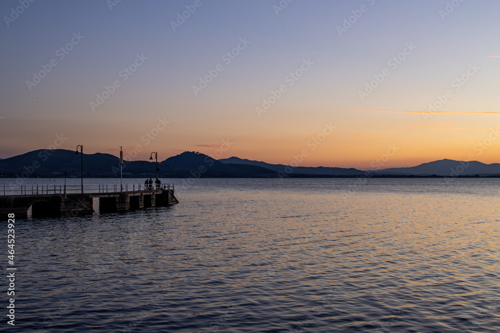 Lake with jetty at sunset. Relaxing Italian landscape at sunset in autumn. Trasimeno lake at sunset