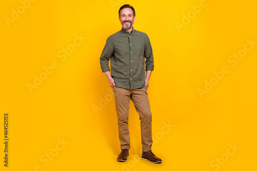 Full length body size view of attractive cheerful man employer holding hands in pockets isolated over vivid yellow color background