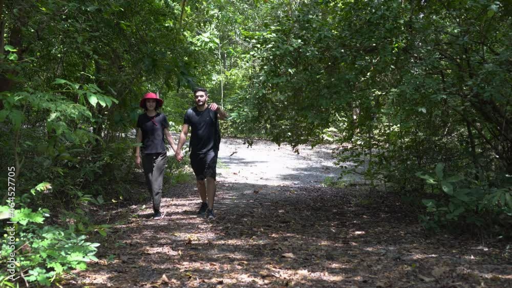 happy young Couple walking through forest in nature park together . Young girlfriend and boyfriend backpack hiking Along Woodland happy young Couple walking through forest in nature park together . Young girlfriend and boyfriend backpack hiking Along Woodland