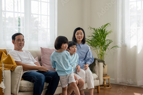 Asian family sitting on a gray fabric sofa in the living room with white curtains.