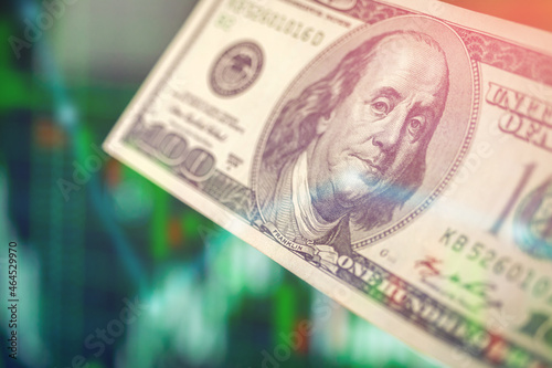 Business investment and stock market. Close-up view of hand holding dollars banknote on green stock chart financial graphs background. Economic growth, currency exchange concept photo