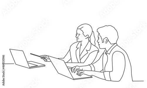 Man writing while sitting in his office. Woman points with pen to laptop.