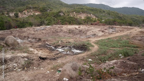 Narrow beaten path leads to picturesque mountains in forested area of Vietnam with scorched earth without grass and stones on sides