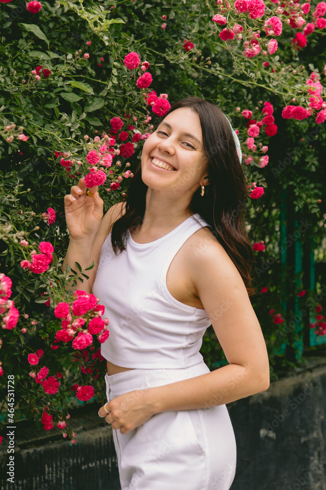 young pretty smiling woman near blooming red roses bush