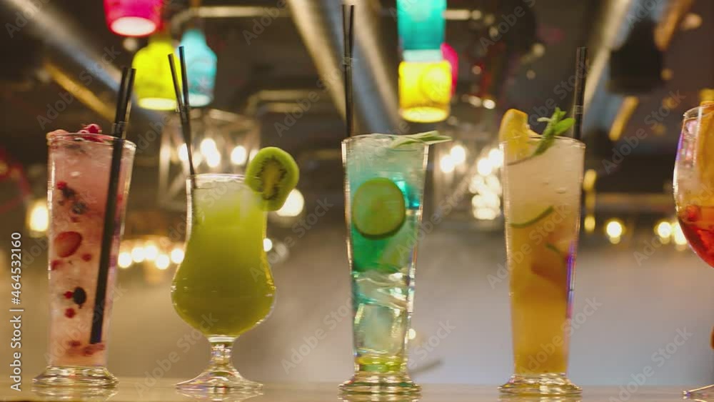Professional barman decorates a cocktail with fruits. Bartender prepares many cocktails at the beautiful bar pub and serves a cocktail. Barman preparing colorful cocktails. Hand putting glas on table