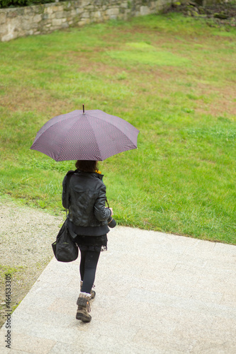 Photographer walking in the rain with backpack and camera, dressed in black and with umbrella