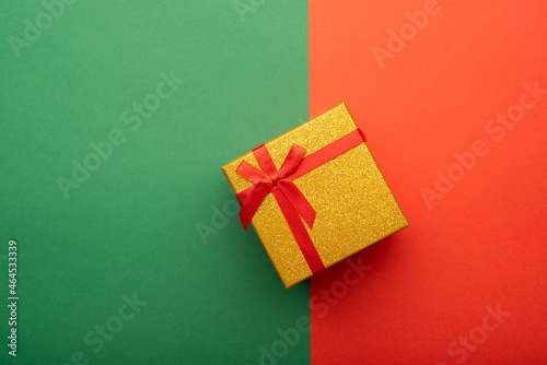 Gold gift box with red ribbon on bright green and red background.  Flat lay, top view