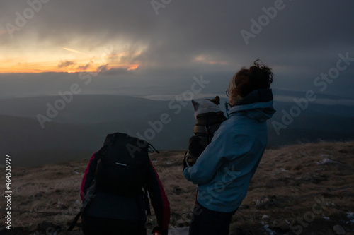 woman tourist with a dog in her hands admires the autumn dawn on the top of the mountain above the clouds. karkonosze. karkonoski park narodowy. snezka photo