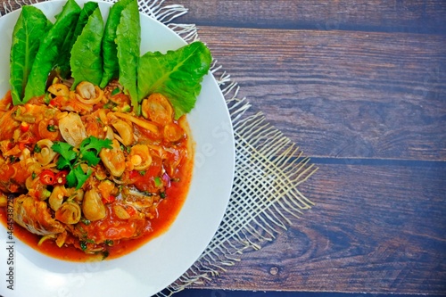 Spicy canned sardines salad (Yum Pla Krapong) in white plate on wooden table. Authentic Thai food. photo