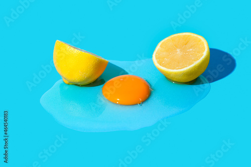 Lemon cut in half on pastel blue background with raw egg. Minimal composition.