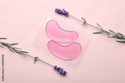 Fotografia Package with under eye patches and lavender flowers on light pink background, flat lay