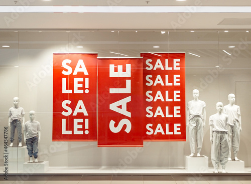Sale sign on red banners with mannequins in window display of fashion shop store, black friday sale in promo showcase