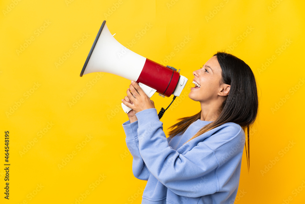 Caucasian girl isolated on yellow background shouting through a megaphone to announce something in lateral position Caucasian girl isolated on yellow background shouting through a megaphone to announce something in lateral position