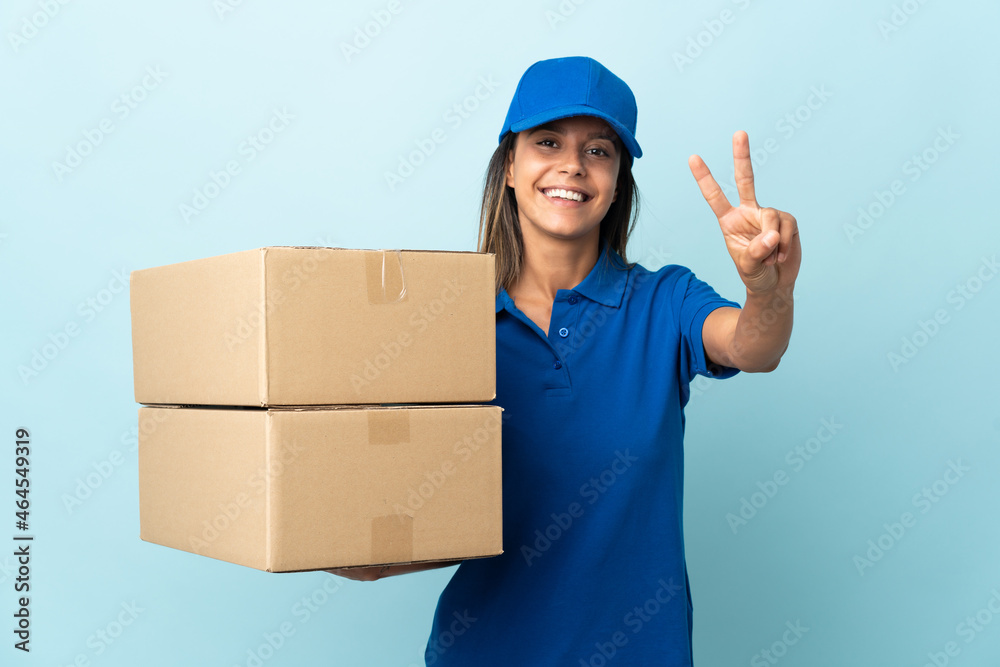 Young delivery woman isolated on blue background smiling and showing victory sign Young delivery woman isolated on blue background smiling and showing victory sign