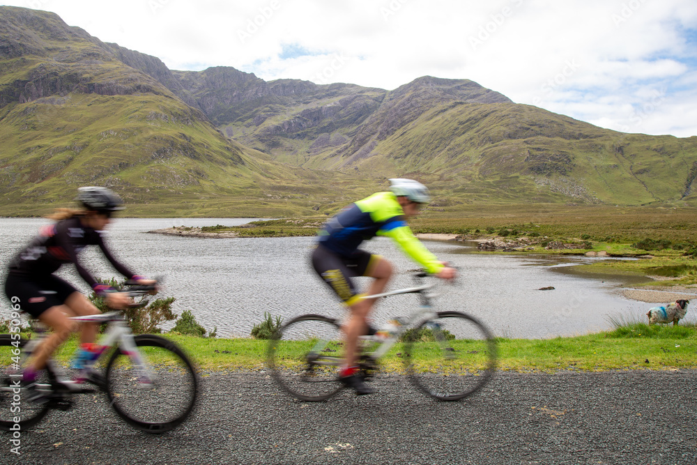 Fototapeta premium Blurred cyclists on road R335, by the lakeside of Doo Lough, County Mayo, Ireland
