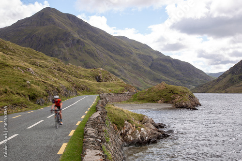 Blurred cyclist on the road R335, on the lakeside of Doo Lough, with Ben Gorm in the background, County Mayo, Ireland