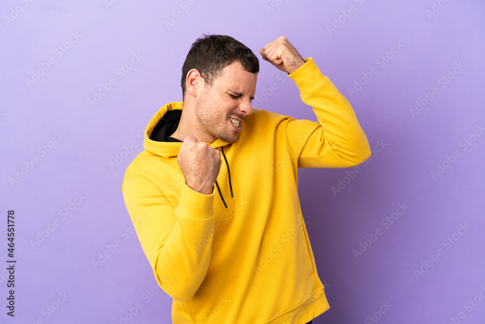 Brazilian man over isolated purple background celebrating a victory