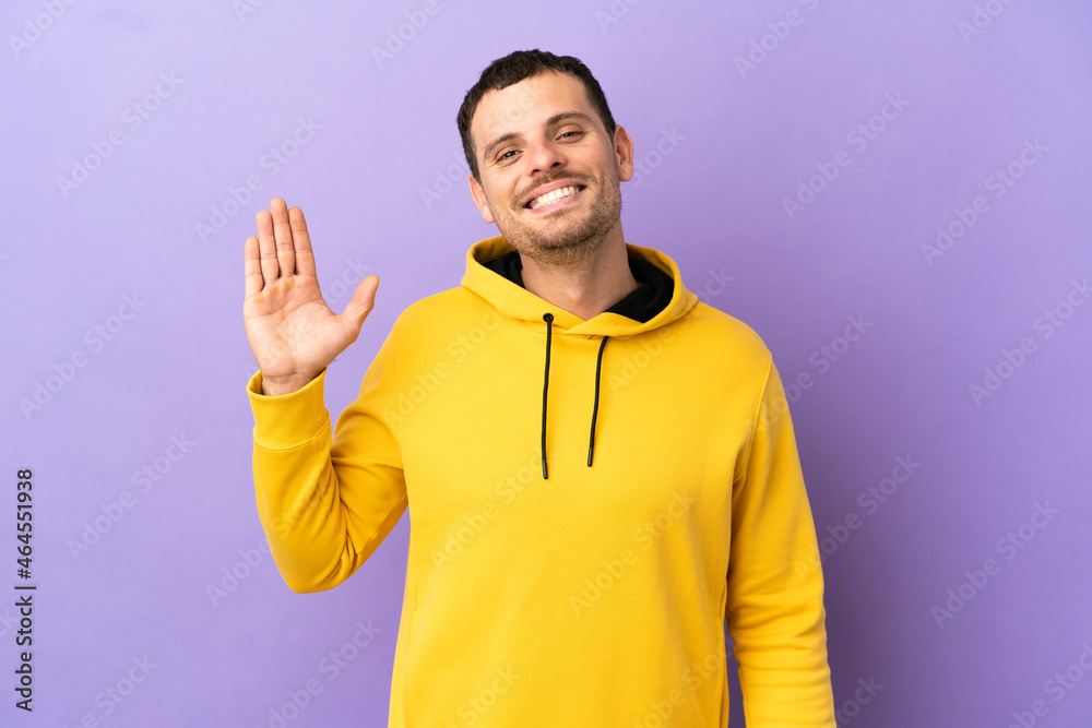Brazilian man over isolated purple background saluting with hand with happy expression Brazilian man over isolated purple background saluting with hand with happy expression