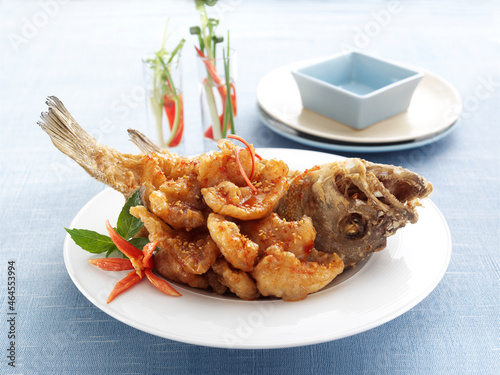 Deep fried crispy grouper fish with spicy chilli sauce in white plate on light blue tablecloth background.