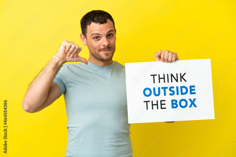 Brazilian man over isolated purple background holding a placard with text Think Outside The Box with proud gesture Brazilian man over isolated purple background holding a placard with text Think Outside The Box with proud gesture