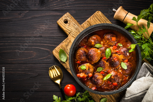 Meatballs in tomato sauce on dark wooden table with ingredients. Top view with copy space.