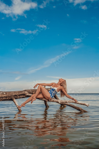 Woman dancer blonde long hair beautiful body in beautiful swimsuit on a tree by the sea