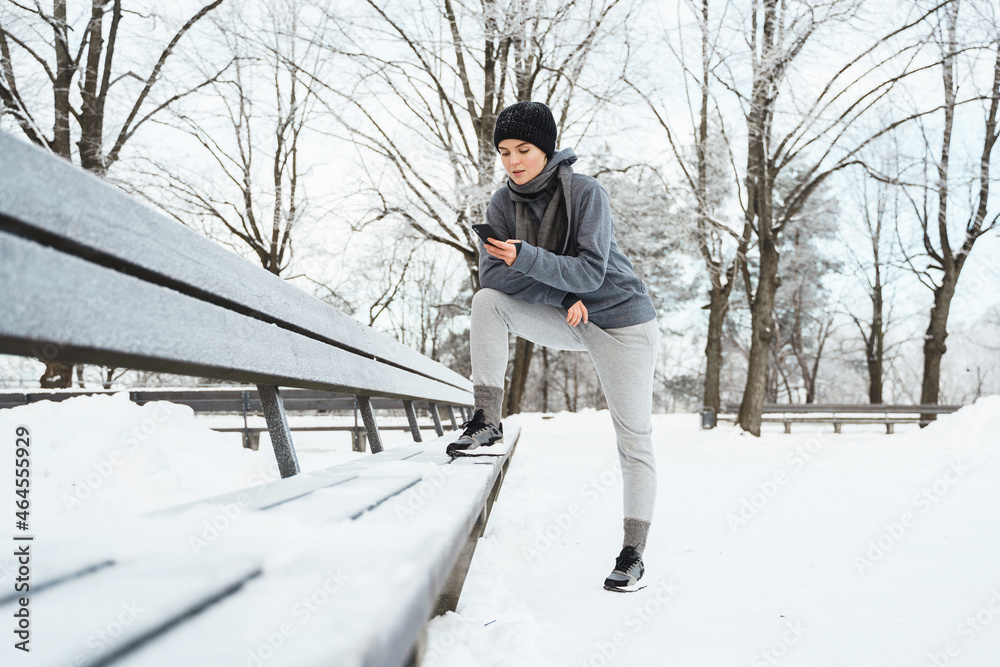 Woman athlete using smartphone during her winter workout in snowy city park