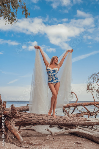 Woman dancer blonde long hair beautiful body in beautiful swimsuit on a tree by the sea