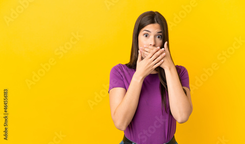 Teenager Brazilian girl over isolated yellow background covering mouth with hands © luismolinero