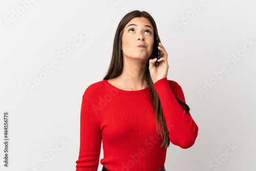 Teenager Brazilian girl using mobile phone over isolated white background and looking up