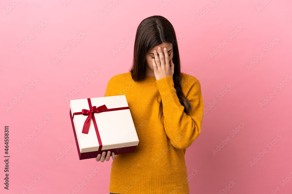 Teenager Brazilian girl holding a gift over isolated pink background with tired and sick expression