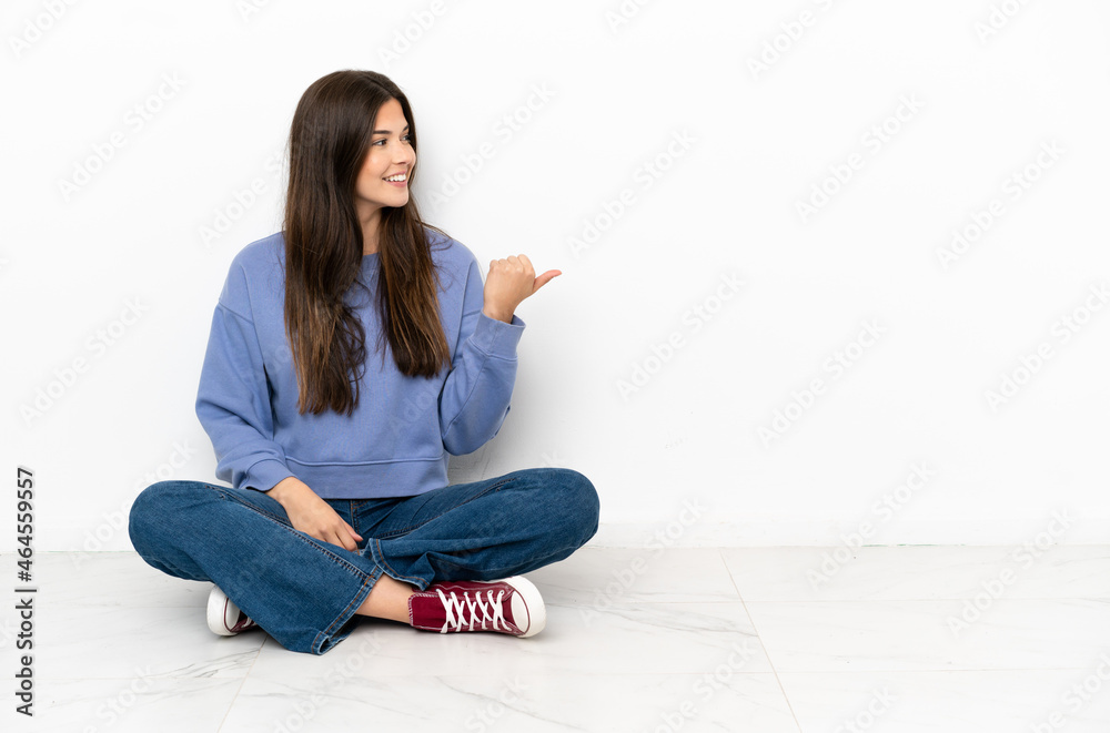 Young woman sitting on the floor pointing to the side to present a product