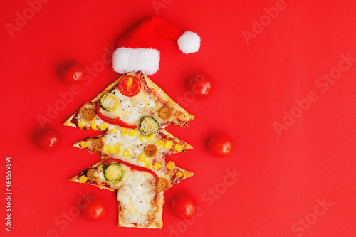 Delicious vegetarian Christmas tree pizza with tomatoes, vegetables and cheese on red background. Creative, funny food concept for kids. Top view, flat lay. Copy space. 