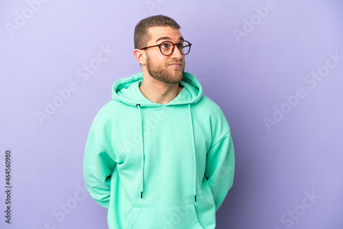 Young handsome caucasian man isolated on purple background and looking up © luismolinero