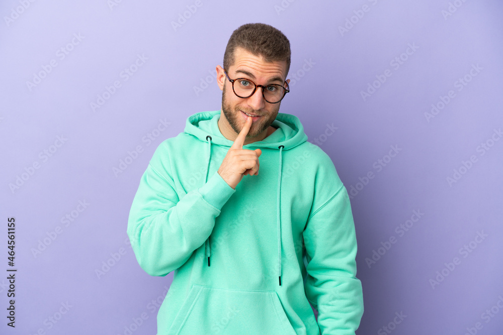 Young handsome caucasian man isolated on purple background showing a sign of silence gesture putting finger in mouth