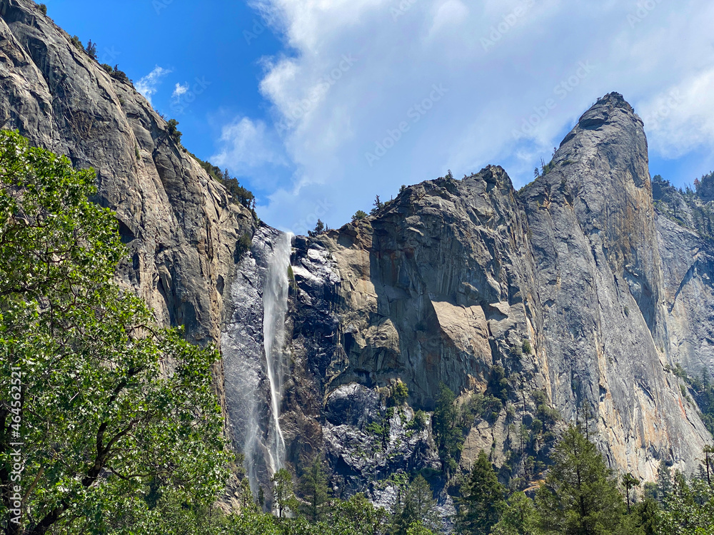 tall mountain ridge with flowing waterfall with trees and blue cloudy sky in Yosemite national park