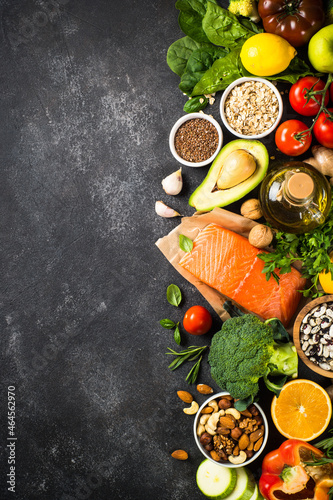 Healthy food products, vegetarian food. Salmon fish, beans, nuts, greens and vegetables. Top view image at black stone table with space for design.