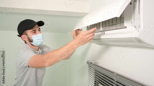 handsome young man electrician cleaning air filter on an indoor unit of air conditioning system in client house