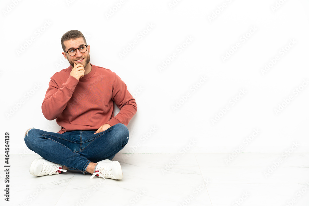 Young handsome man sitting on the floor looking to the side Young handsome man sitting on the floor looking to the side