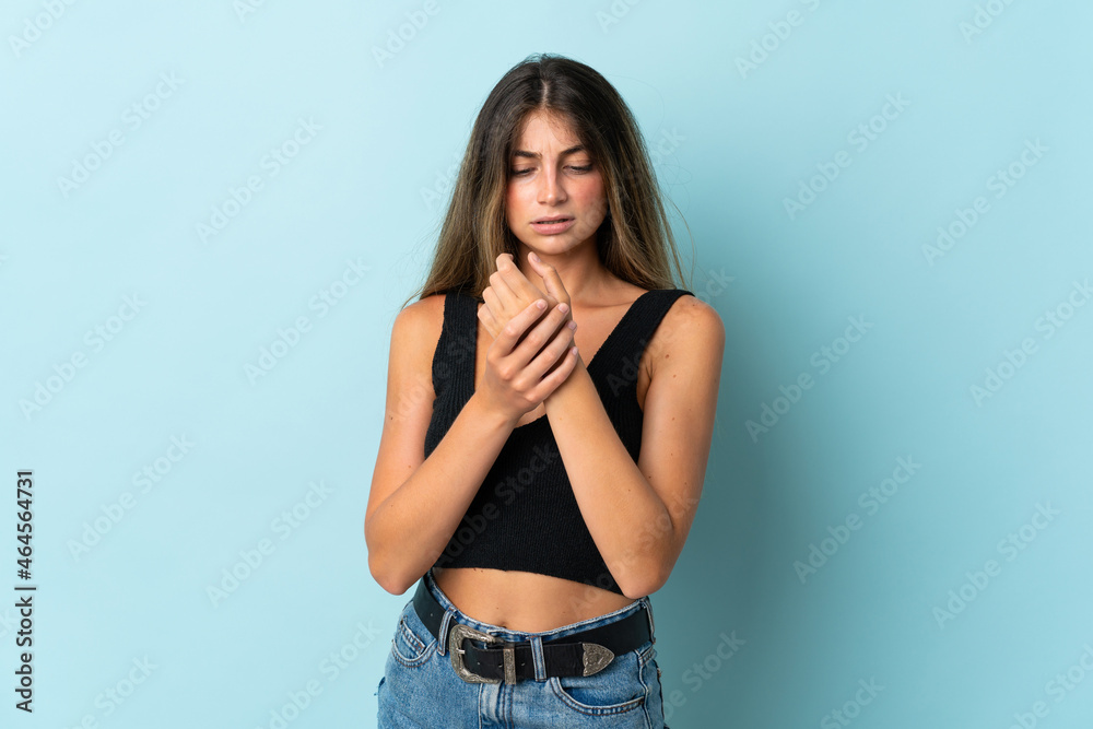 Young caucasian woman isolated on blue background suffering from pain in hands