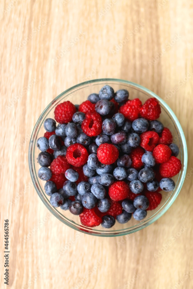 Glass bowl filled with raspberries and blueberries on wooden table. Top view. Glass bowl filled with raspberries and blueberries on wooden table. Top view.