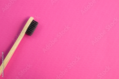 Wooden bamboo toothbrush with black bristles. Natural eco friendly zero waste item on pink background