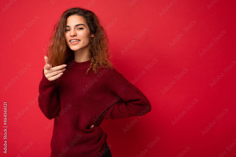 Young positive happy beautiful brunette curly woman with sincere emotions wearing casual red pullover isolated on red background with copy space Young positive happy beautiful brunette curly woman with sincere emotions wearing casual red pullover isolated on red background with copy space