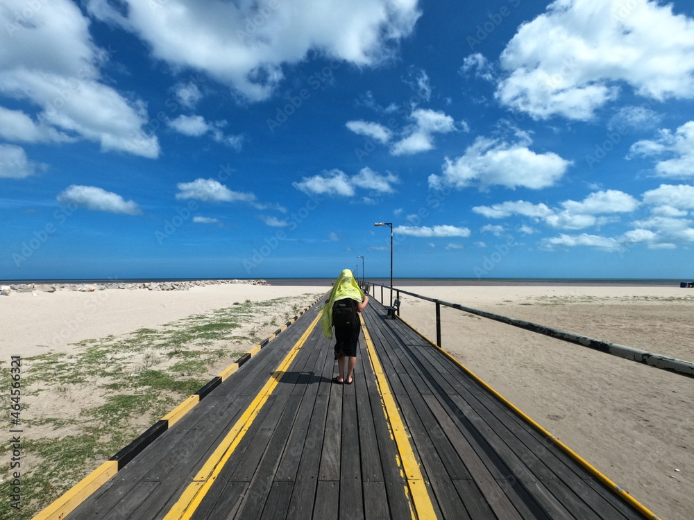 Woman walking on pier at beach under blue sky