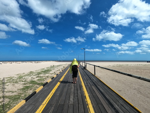 Woman walking on pier at beach under blue sky © Nandofilms
