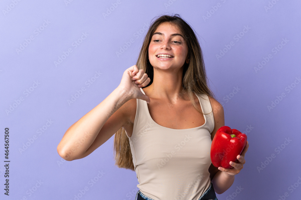 Young woman holding a pepper isolated on purple background proud and self-satisfied Young woman holding a pepper isolated on purple background proud and self-satisfied
