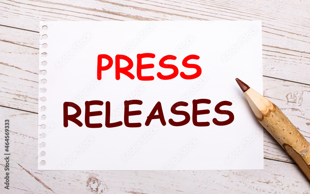 On a light wooden background, a colored pencil and a white sheet of paper with the text PRESS RELEASES On a light wooden background, a colored pencil and a white sheet of paper with the text PRESS RELEASES